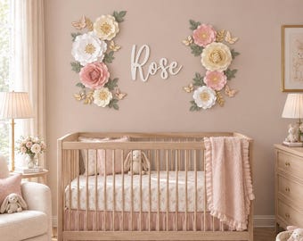 May include: A wooden crib with a light wood finish, featuring a pink ruffled blanket and a floral patterned sheet. Above the crib, the name Rose is displayed in white script lettering, flanked by two arrangements of paper flowers and butterflies.
