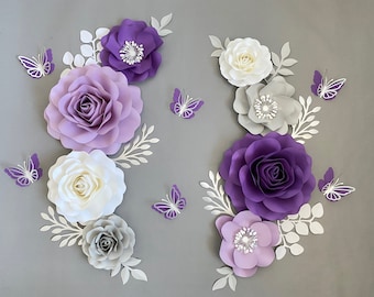 May include: A set of paper flowers in shades of purple, white, and gray, with butterflies. The flowers are arranged in a symmetrical pattern on a gray background.