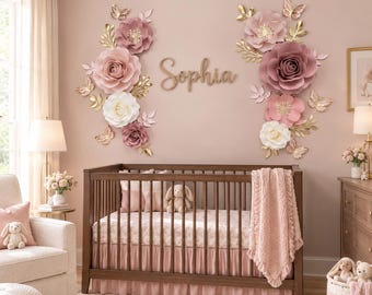 May include: A dark wood baby crib with a pink ruffled skirt and a textured pink blanket, positioned against a wall decorated with large paper flowers in shades of pink and white, gold butterflies, and the wooden script name Sophia.