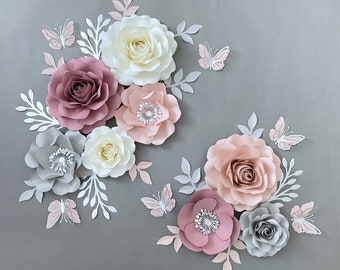 May include: A set of paper flowers in shades of pink, white, and gray, with butterflies. The flowers are arranged in a cluster, with the largest flower in the center. The flowers are made of paper and have a delicate, layered look. The butterflies are also made of paper and are in shades of pink and white.
