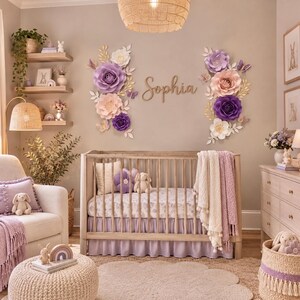 May include: A nursery room featuring a wooden crib with a light purple skirt, a white patterned sheet, and a textured blanket. The wall displays large paper flowers in shades of purple, pink, and white, with the name Sophia in wooden script.