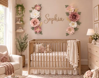 May include: A wooden baby crib with a white ruffled skirt and a cream-colored knit blanket. Above the crib, the name Sophia is written in wooden script letters, flanked by two large arrangements of pink and white paper flowers.