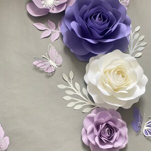 May include: A collection of handcrafted paper flowers and butterflies in shades of purple, lavender, and white. The arrangement includes large layered roses and smaller blossoms, accented by delicate paper leaves and butterfly cutouts.