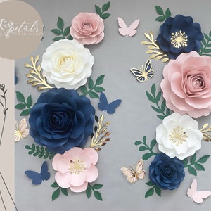 Puede incluir: Un conjunto de decoraci&oacute;n de pared con flores de papel en tonos rosa, blanco y azul marino. Las flores est&aacute;n dispuestas en un racimo con detalles dorados y hojas verdes. Tambi&eacute;n hay varias mariposas en rosa y azul.