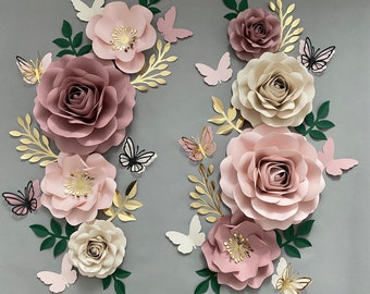 May include: A wall decor set featuring paper flowers in shades of pink and cream with gold accents. The flowers are arranged in a cluster with butterflies scattered throughout.