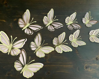May include: Ten pink and gold butterfly cutouts on a dark wood background. The butterflies are all different sizes and shapes.