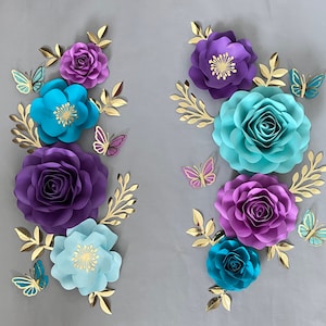 May include: A decorative wall arrangement featuring paper flowers in shades of purple, teal, and blue. The flowers are accented with gold glitter and butterflies.