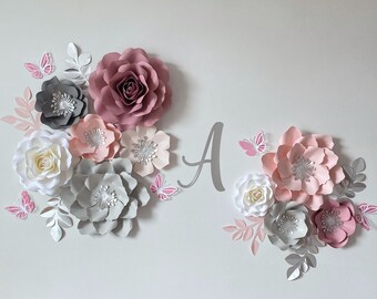 May include: A wall display featuring a large letter A in silver, surrounded by various paper flowers in shades of dusty rose, light pink, white, and gray. The arrangement includes several small pink and white paper butterflies and silver leaves.