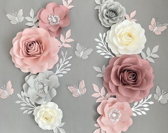 May include: A set of paper flowers in shades of pink, white, and gray. The flowers are arranged in a symmetrical pattern on a gray background. There are also several paper butterflies in the image.