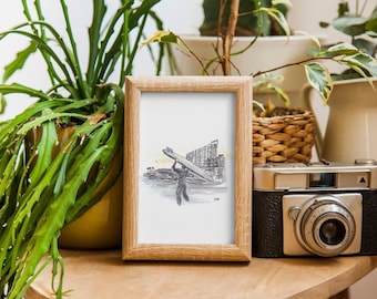 May include: A framed watercolor print depicts a person carrying a surfboard, set against a cityscape. The artwork is in a light wooden frame, displayed with a vintage camera and potted plants. The color palette includes shades of gray, beige, and green.