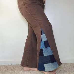 May include: Brown pants featuring a side slit with a patchwork denim insert. The insert is composed of various shades of blue denim squares. The pants have a white drawstring at the waist and a classic five-pocket design with visible stitching.
