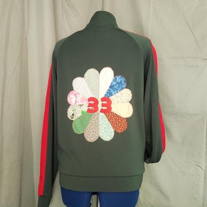 May include: Dark green track jacket with red stripes down the sleeves. A flower-shaped patch on the back features various patterned fabric petals and the number "33" in red.
