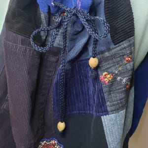 Może przedstawiać: Worek ze ściągaczem wykonany z patchworku niebieskich i czarnych tkanin sztruksowych oraz dżinsowych. Torba posiada podszewkę w niebieski wz&oacute;r bandany, ciemnoniebieskie plecione zapięcie ze sznurka z drewnianymi koralikami oraz haftowaną naszywkę.