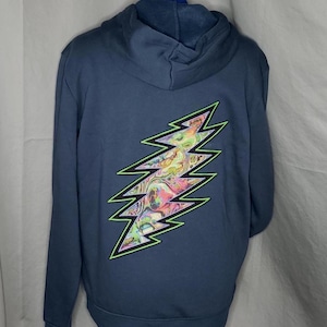 May include: Navy blue hoodie with a vibrant, psychedelic lightning bolt design on the back. The lightning bolt features a neon green outline and a colorful, swirling pattern. The hoodie has a hood and long sleeves.