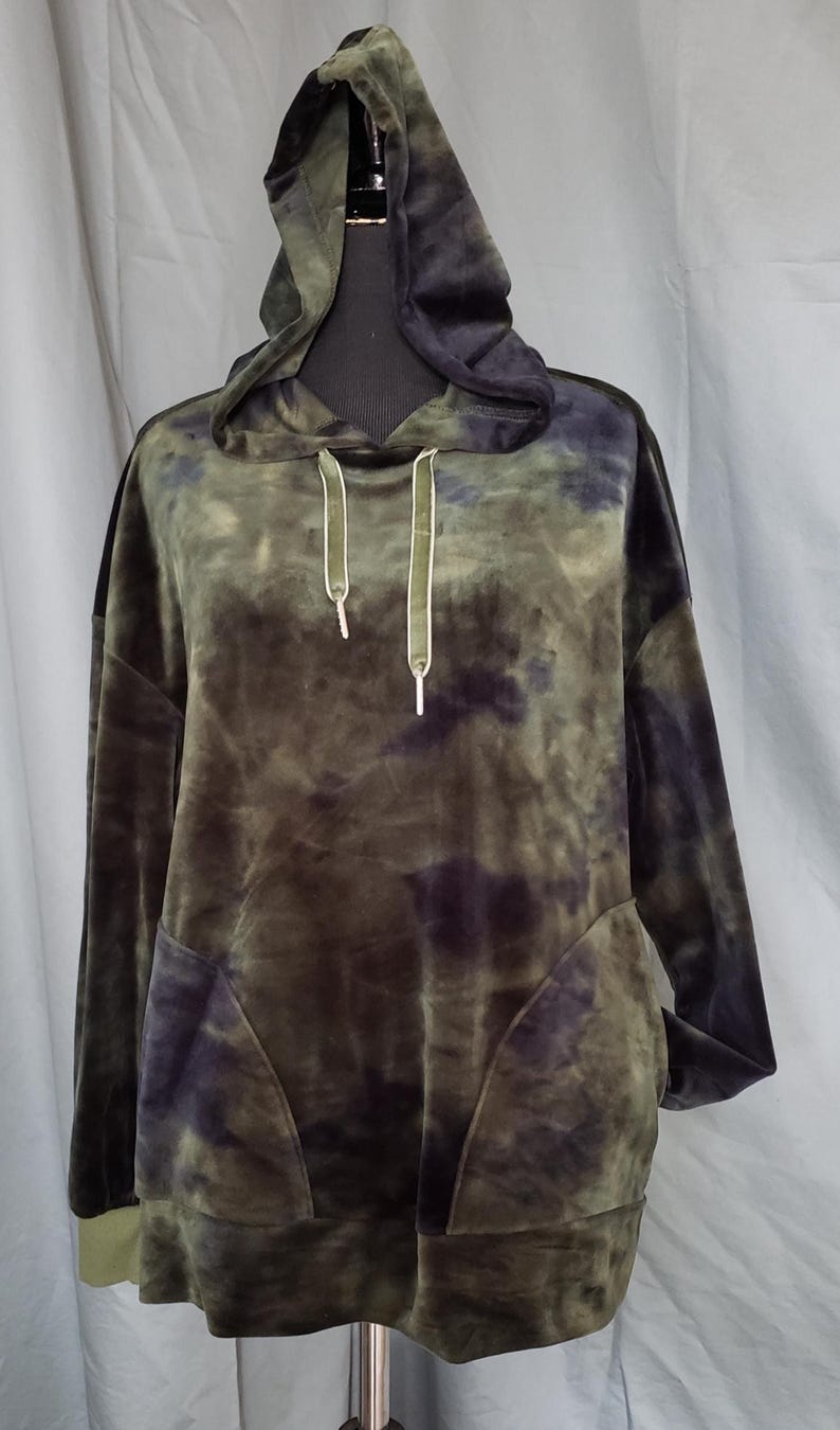 Pode incluir: Um moletom verde e roxo tie-dye com capuz com cord&atilde;o e bolso frontal. O moletom de manga comprida &eacute; feito de um material macio e aveludado. O moletom com capuz &eacute; exibido em um manequim preto.
