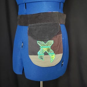 May include: A handmade belt bag with a black corduroy pocket and a brown, gray, and black patchwork design. The bag features a green and blue geometric applique and a wide black belt.