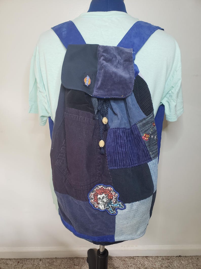 Może przedstawiać: Plecak patchwork wykonany z r&oacute;żnych odcieni niebieskiego sztruksu i dżinsu. Torba posiada zapięcie na sznurek z drewnianymi koralikami, klapę z naszywką z logo Dickies oraz naszywkę z grafiką czaszki i r&oacute;ży na przedniej części.