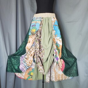 May include: A patchwork skirt featuring a variety of fabrics and patterns. The skirt includes panels with cartoon characters, floral prints, and solid green fabric. The hemline has a dark green, textured fabric. The skirt is displayed on a mannequin.