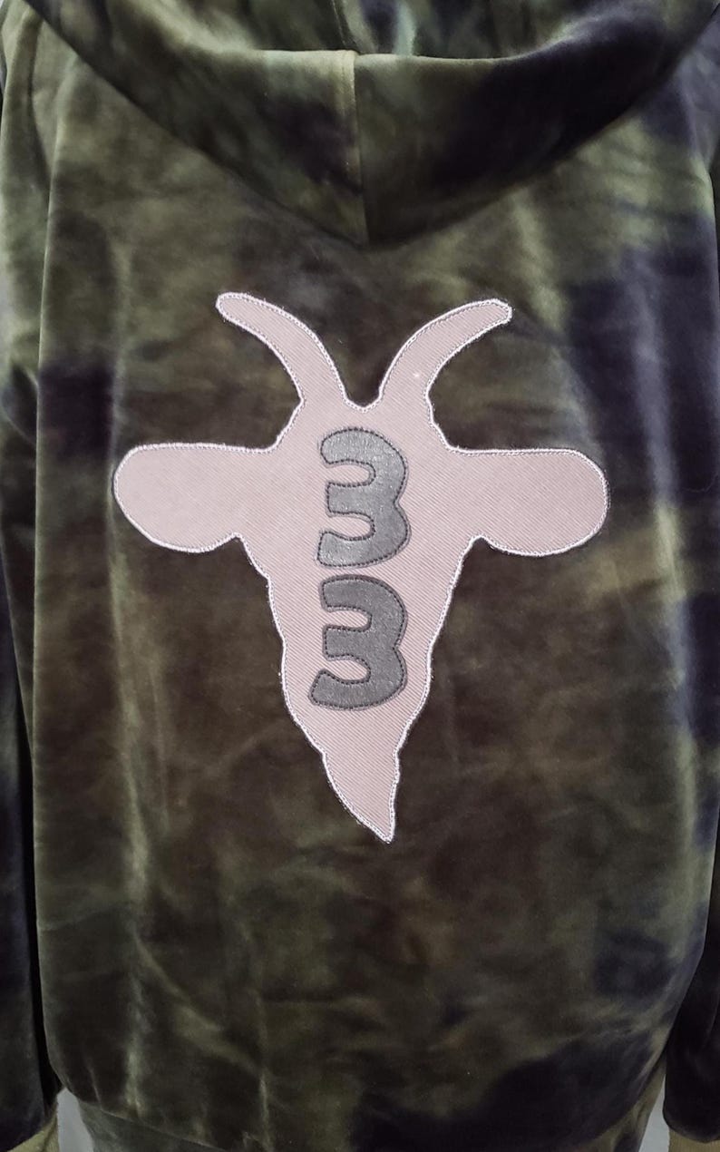 Pode incluir: Moletom tie-dye verde e preto com um logotipo de cabe&ccedil;a de cabra nas costas. O logotipo &eacute; de cor bege claro com o n&uacute;mero "33" em cinza. O moletom tem capuz e uma textura macia e aveludada.