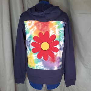 May include: Navy blue hoodie with a large red and yellow flower design on the back. The flower is centered on a tie-dye background of various colors. The hoodie has a drawstring hood and long sleeves.