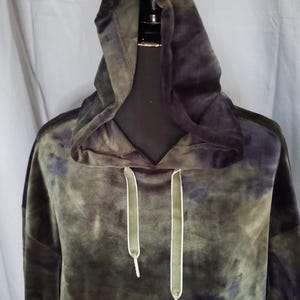 Pode incluir: Um moletom verde e azul marinho tie-dye com capuz com cord&atilde;o. O moletom &eacute; feito de um material macio e aveludado. Os cord&otilde;es s&atilde;o verde-oliva com pontas brancas. O moletom &eacute; exibido em um manequim preto.