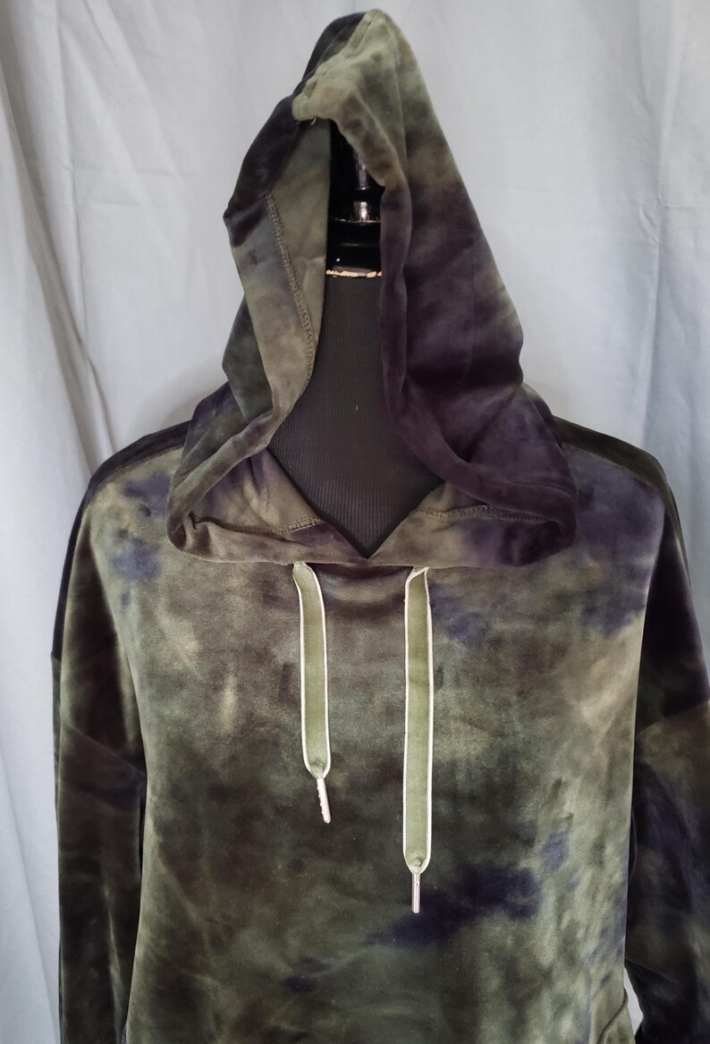 Pode incluir: Um moletom verde e azul marinho tie-dye com capuz com cord&atilde;o. O moletom &eacute; feito de um material macio e aveludado. Os cord&otilde;es s&atilde;o verde-oliva com pontas brancas. O moletom &eacute; exibido em um manequim preto.
