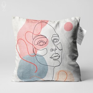 May include: A white pillow featuring a line drawing of a face, surrounded by abstract shapes in pink, blue, and orange.