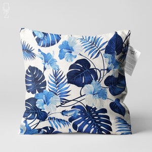 May include: A white cushion with a blue floral pattern featuring hibiscus flowers and tropical leaves. The cushion has a subtle linen texture.