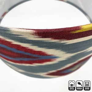 May include: Close-up of a lampshade with a blue, red, and yellow ikat pattern. The lampshade is made of 100% cotton and is hand-woven. The lampshade is also herbally dyed.