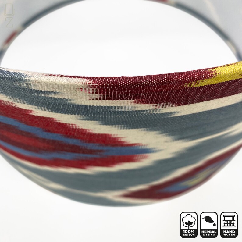 May include: Close-up of a lampshade with a blue, red, and yellow ikat pattern. The lampshade is made of 100% cotton and is hand-woven. The lampshade is also herbally dyed.