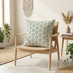 Square blue botanical block print cushion cover on a modern wooden armchair in a minimalist living room setting with plants.