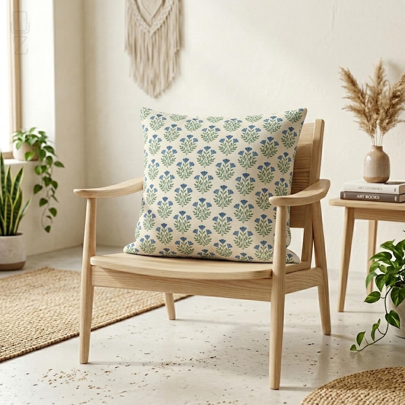 Square blue botanical block print cushion cover on a modern wooden armchair in a minimalist living room setting with plants.