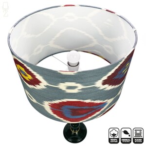 May include: A gray and white lampshade with a red, blue, and yellow ikat pattern. The lampshade is made of 100% cotton and is hand-woven. The lampshade is sitting on a black lamp base.