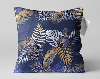 Könnte beinhalten: Ein marineblaues Kissen mit einem goldenen und weißen tropischen Blattmotiv. Das Kissen hat einen dezenten Glanz und eine weiche, plüschige Textur.