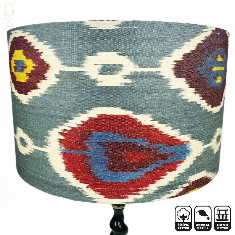 May include: A blue and red patterned lampshade with a black wooden base. The lampshade is made of 100% cotton and is handwoven. The fabric is herbally dyed.