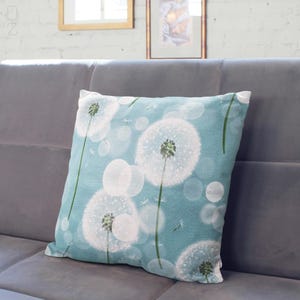 K&ouml;nnte beinhalten: Ein blaues Kissen mit einem wei&szlig;en L&ouml;wenzahnmuster. Das Kissen hat eine weiche, flauschige Textur und ist perfekt, um Ihrem Zuhause einen Hauch von Natur zu verleihen.