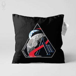May include: Black throw pillow featuring a triangular design with a stylized moon, Earth, and the names GLOVER, WISEMAN, KOCH, and HANSEN. The design includes red, blue, and white accents. A tag is attached to the pillow.