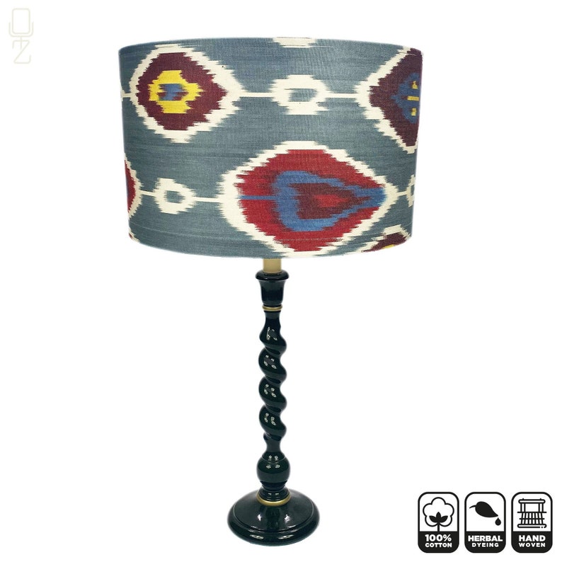 May include: A table lamp with a black twisted wooden base and a blue and red patterned lampshade. The lampshade is made of 100% cotton, hand woven and herbally dyed.