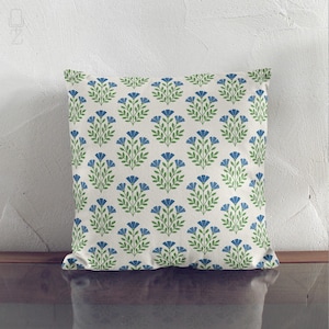 Blue and green wildflower print throw pillow leaning against a white textured wall, showing the elegant block print design.