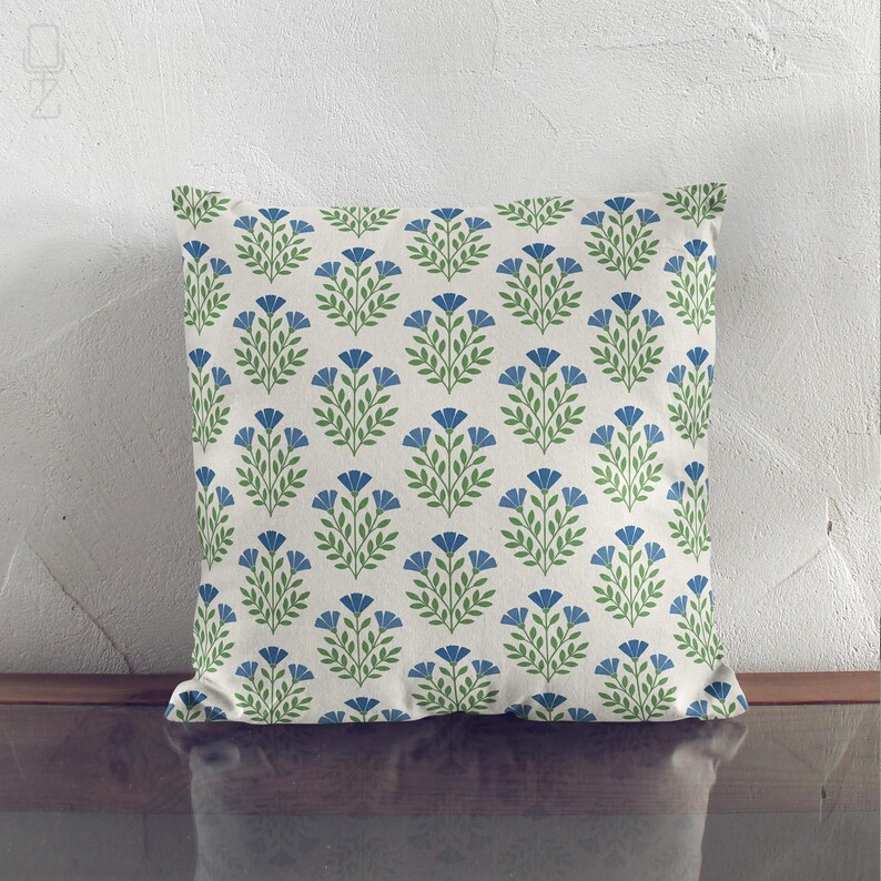 Blue and green wildflower print throw pillow leaning against a white textured wall, showing the elegant block print design.