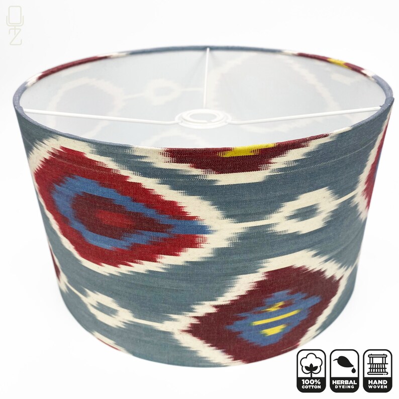 May include: A cylindrical lampshade with a blue, red, and white ikat pattern. The lampshade is made of 100% cotton and is handwoven. It is also herbally dyed.