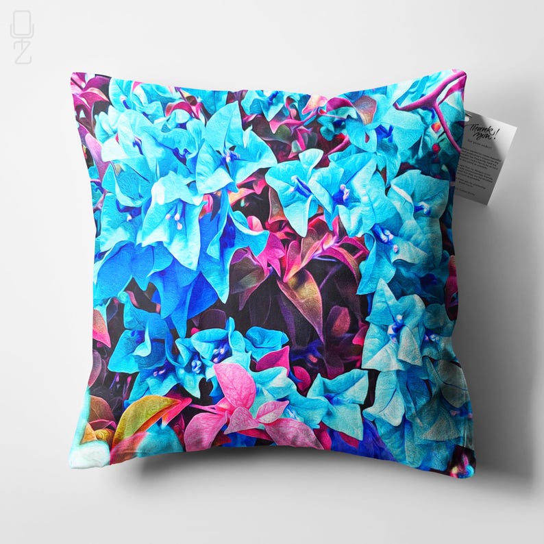 May include: A decorative pillow featuring a vibrant floral pattern with blue and pink flowers. The pillow is made of soft fabric and has a square shape.