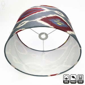 May include: A gray and red patterned lampshade with a white interior. The lampshade is made of 100% cotton and is hand woven. It features a herbal dye.