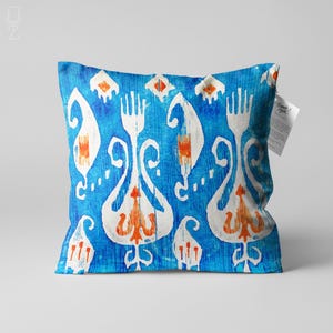 May include: Blue cushion with a white and orange geometric pattern. The cushion has a fringed edge and a tag that says "Thanks! You're great!"