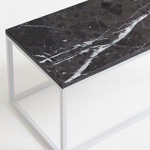 Puede incluir: Mesa de centro rectangular con tapa de mármol negro con vetas blancas. La mesa tiene un diseño minimalista con una estructura de metal blanco. La mesa mide aproximadamente 122 cm de largo, 61 cm de ancho y 41 cm de alto.