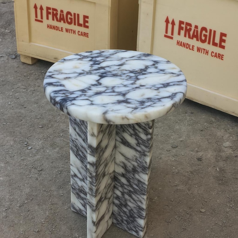 May include: A round marble side table with a white and gray patterned top. The table has a three-legged base with a matching marble pattern. The table is approximately 20 inches in diameter and 20 inches tall.