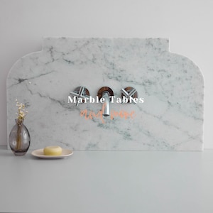 May include: A white marble countertop with a silver faucet and three knobs. The text "Marble Tables and more" is written in the centre of the countertop.