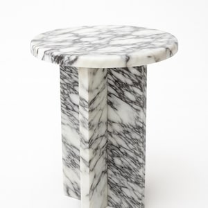 May include: A round marble side table with a white and gray veined pattern. The tabletop is supported by a pedestal base with a cross-shaped design. The table is approximately 20 inches in diameter and 20 inches tall.