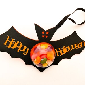 May include: Black bat-shaped Halloween treat bag with orange "Happy Halloween" text and a clear plastic sphere filled with colorful candy.