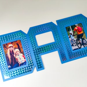 May include: Blue cardstock frame with a holographic finish, shaped like the word "DAD". The frame has three openings for photos, two of which are filled with photos of people.